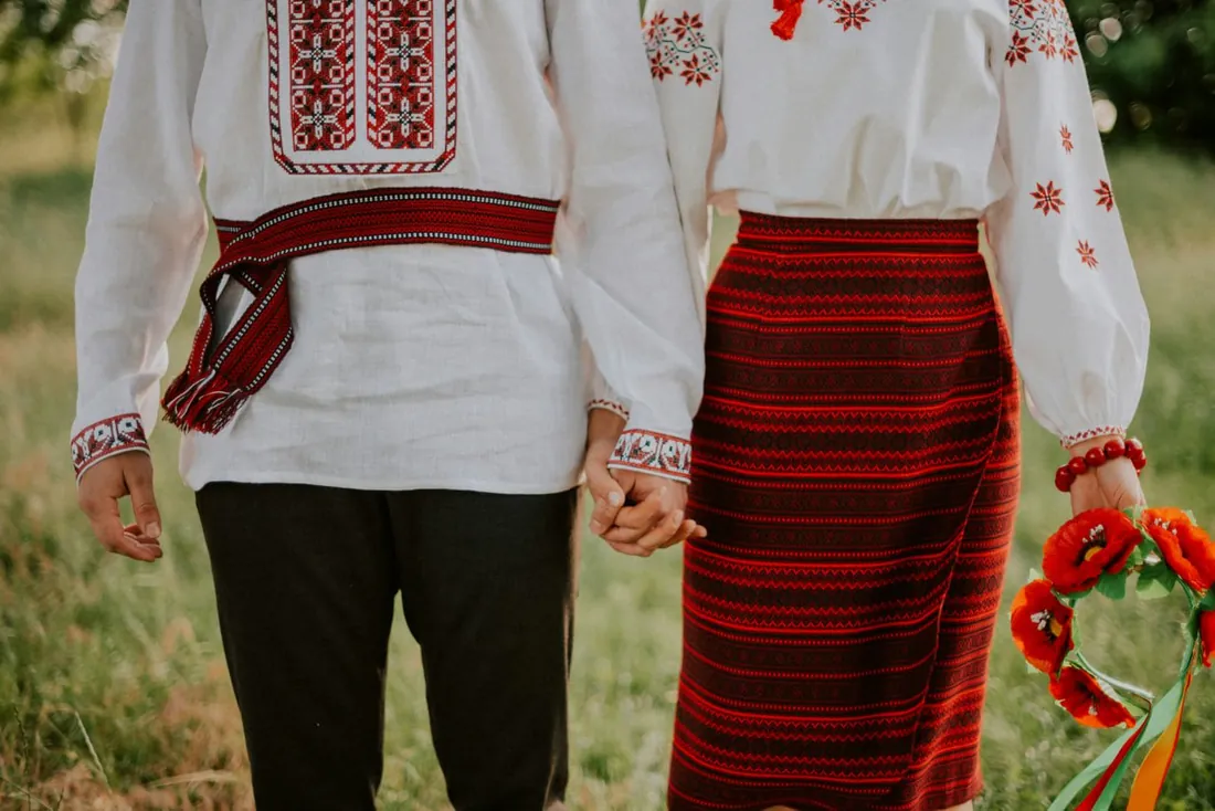 A man and a woman in vyshyvankas with red ornament holding hands, the man with a red belt