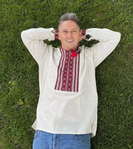 Man in a vyshyvanka with a red ornament and jeans lying on the grass