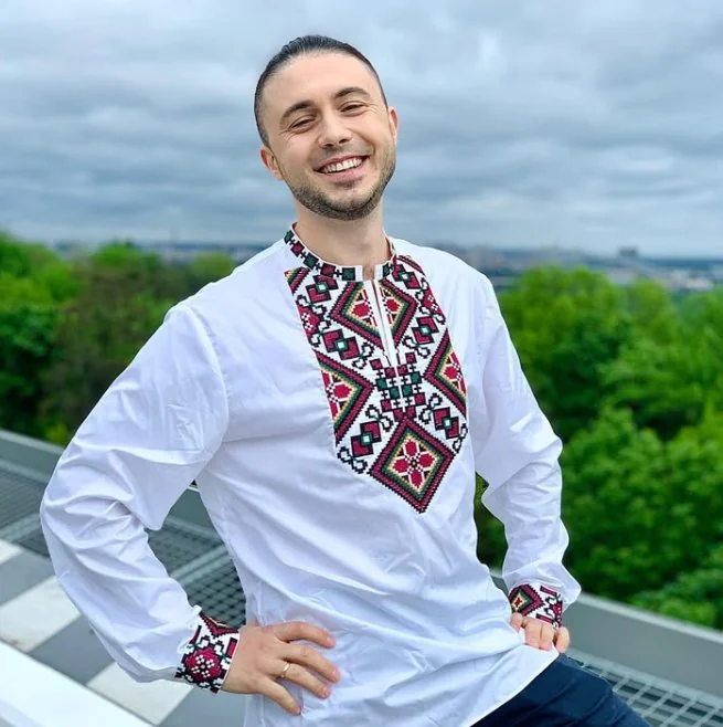Man in a white vyshyvanka with a red and black ornament against trees