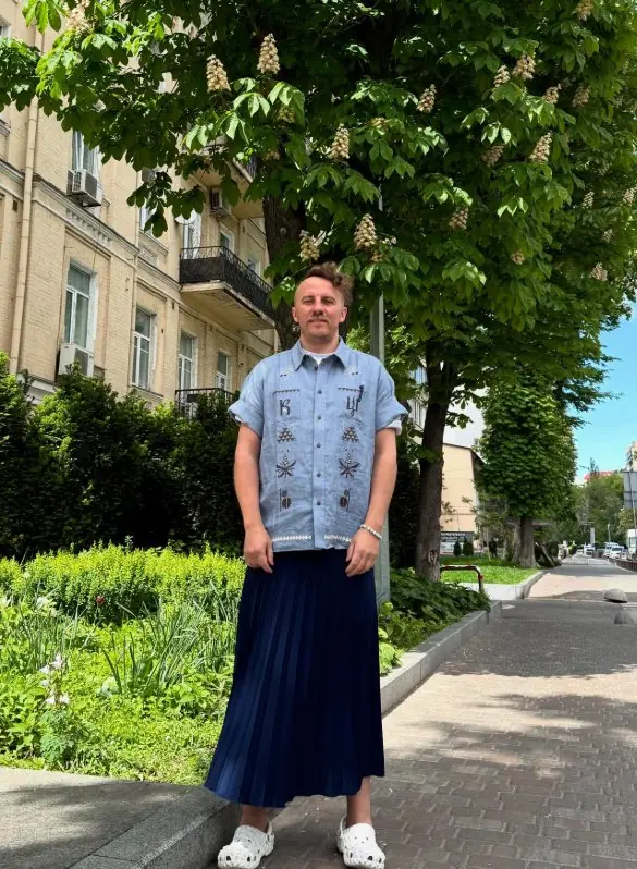 Man in an embroidered shirt and a navy pleated skirt on a city avenue