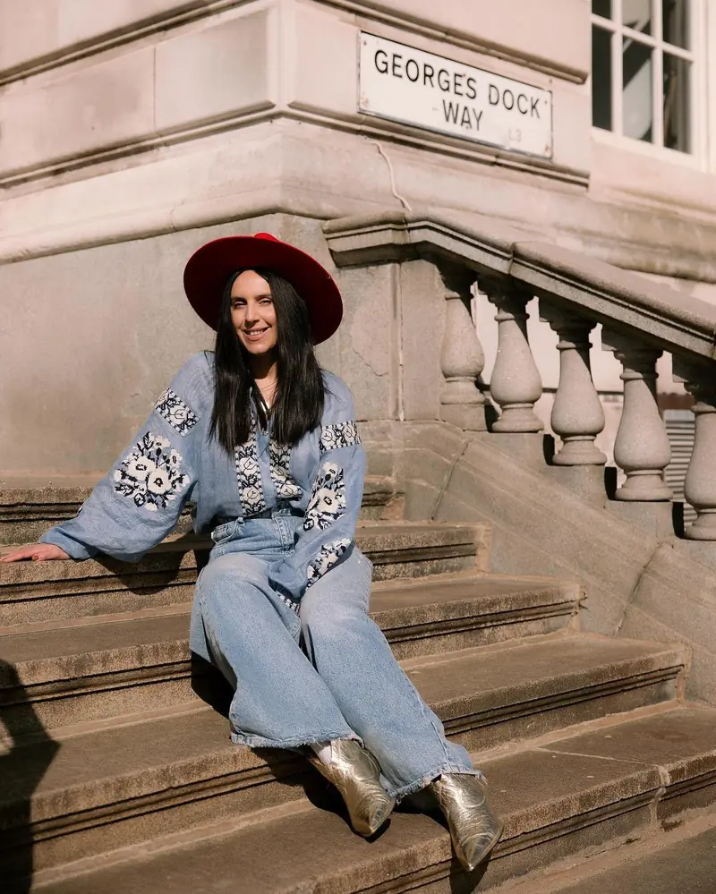 Woman in a vyshyvanka with light blue embroidery, jeans and a red hat on steps