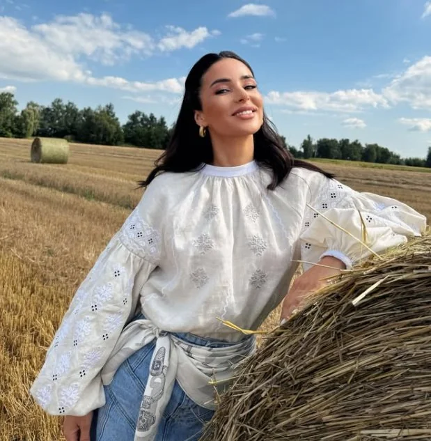Woman in a white vyshyvanka with white embroidery next to a hay bale in a field