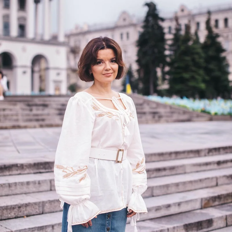 Woman in a white vyshyvanka with a wide belt on steps in front of a building