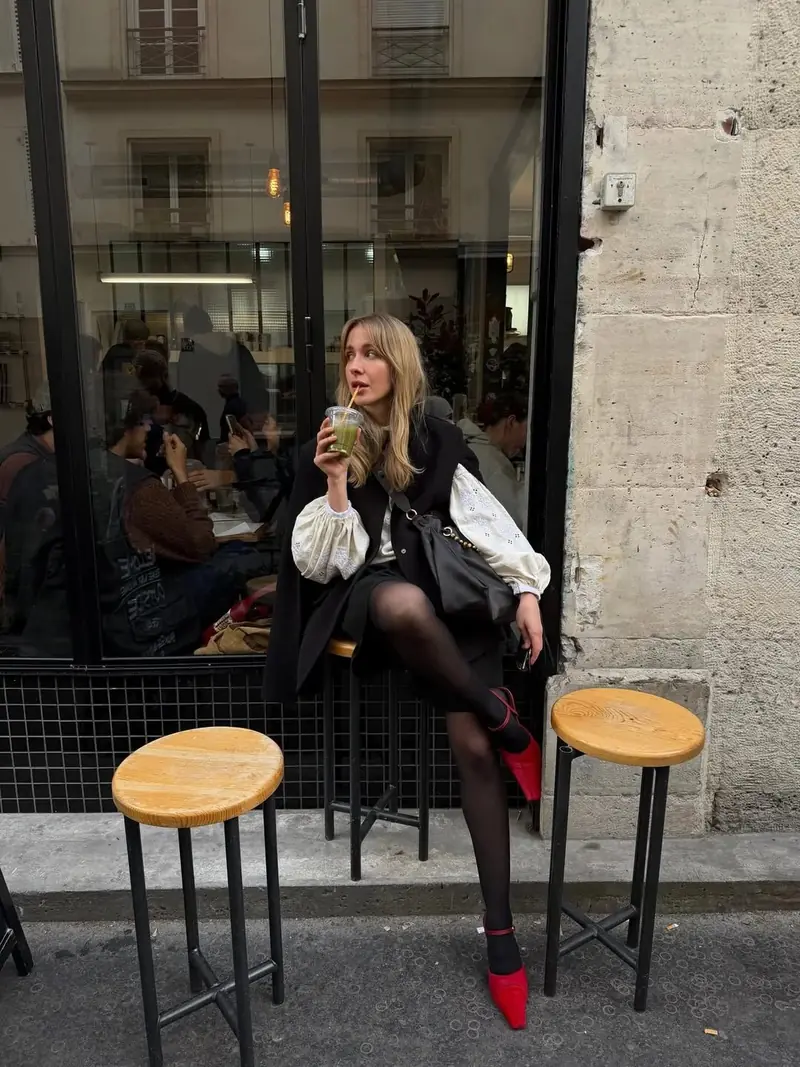 Woman in a white vyshyvanka with a black vest and red shoes outside a café