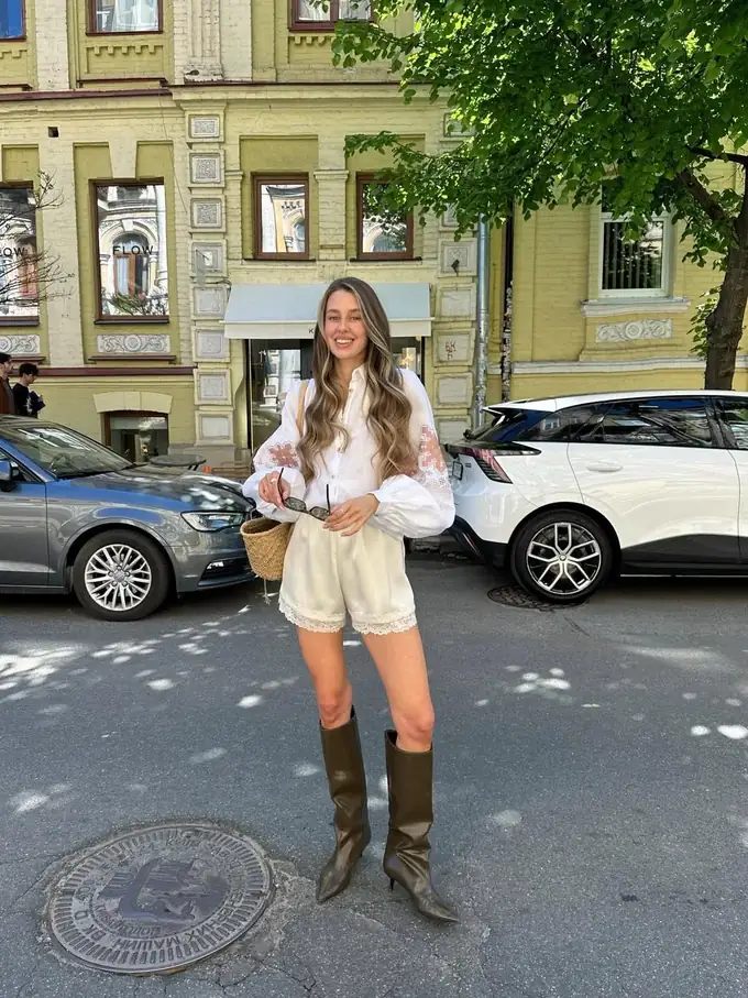 Woman in a white vyshyvanka, shorts and tall boots on a city street