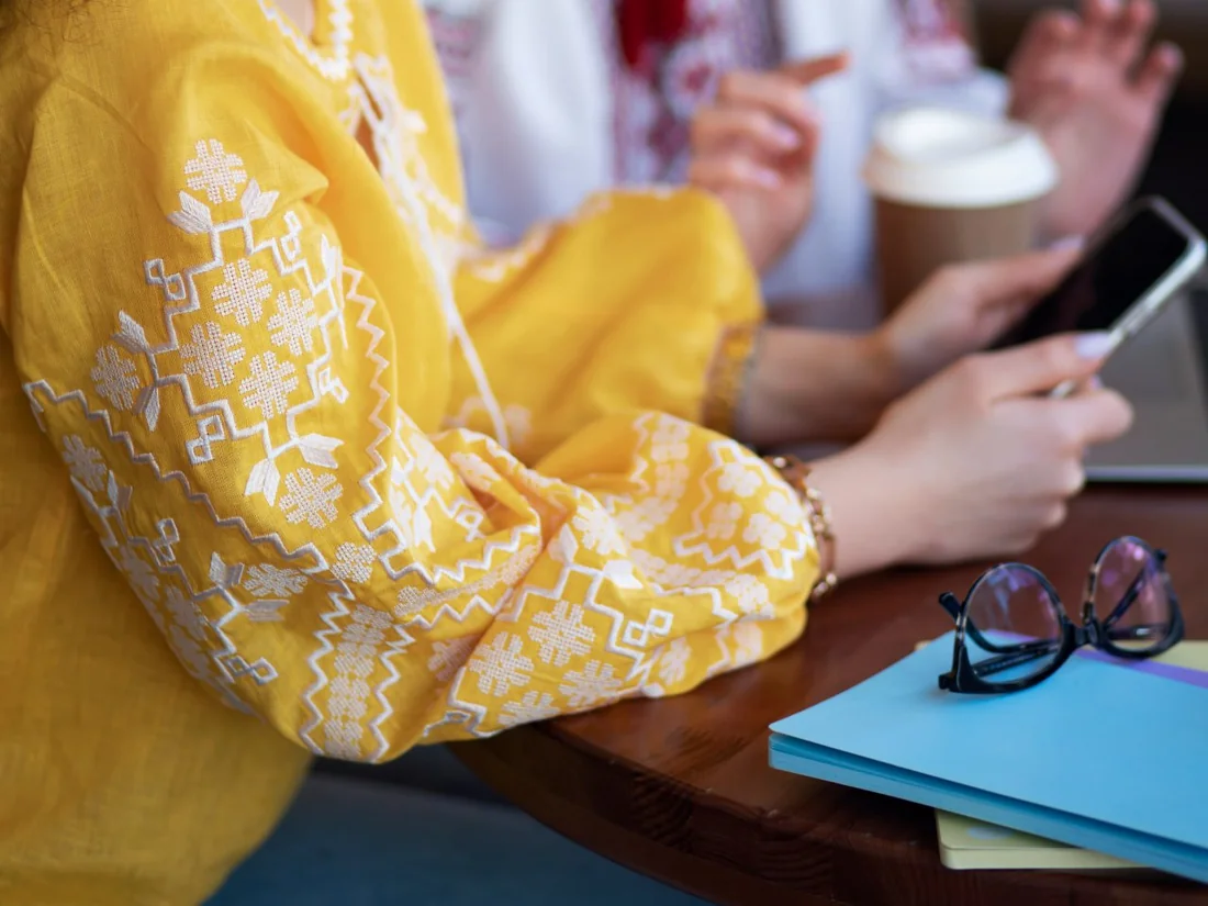 Sleeve of a yellow vyshyvanka with white embroidery next to a cup of coffee on a table